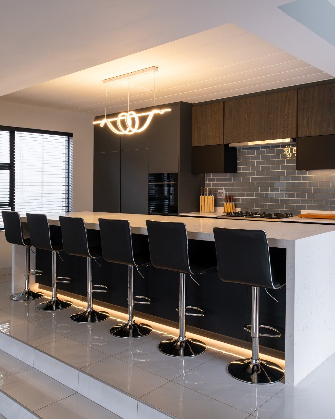 Contemporary kitchen featuring a looping LED chandelier over a white island with black stools.