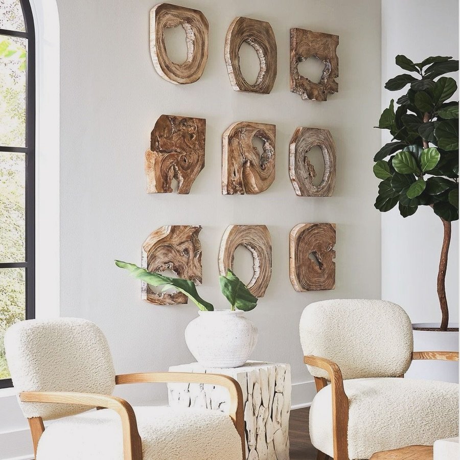 Grid of nine hollow raw wood slices mounted on a white wall behind cream armchairs and plants