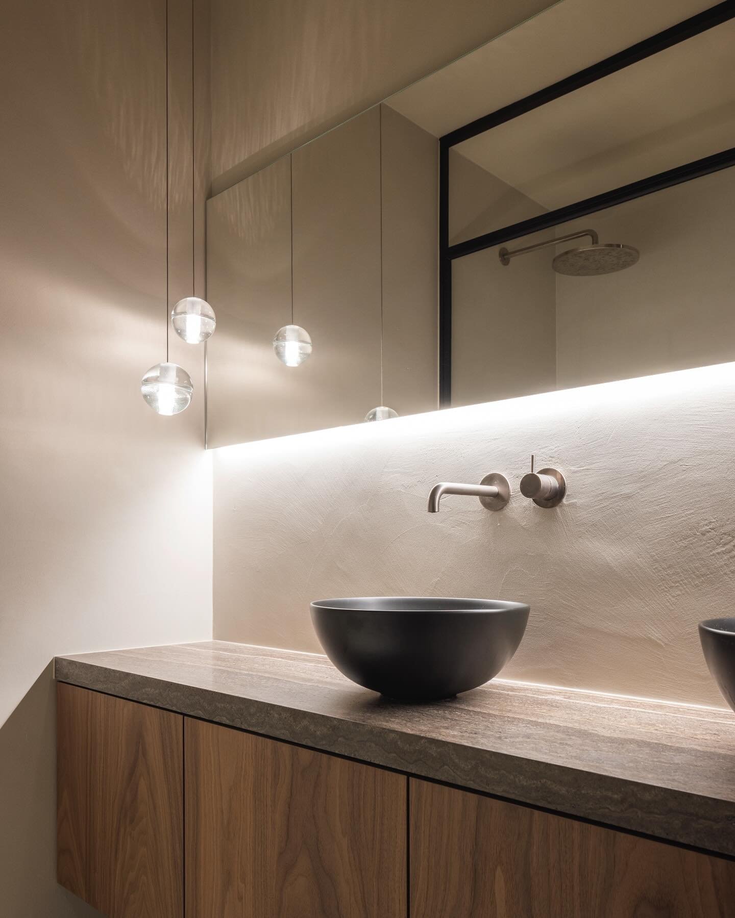 Modern bathroom featuring a backlit mirror cabinet with warm LED light washing over a textured wall and black vessel sink.
