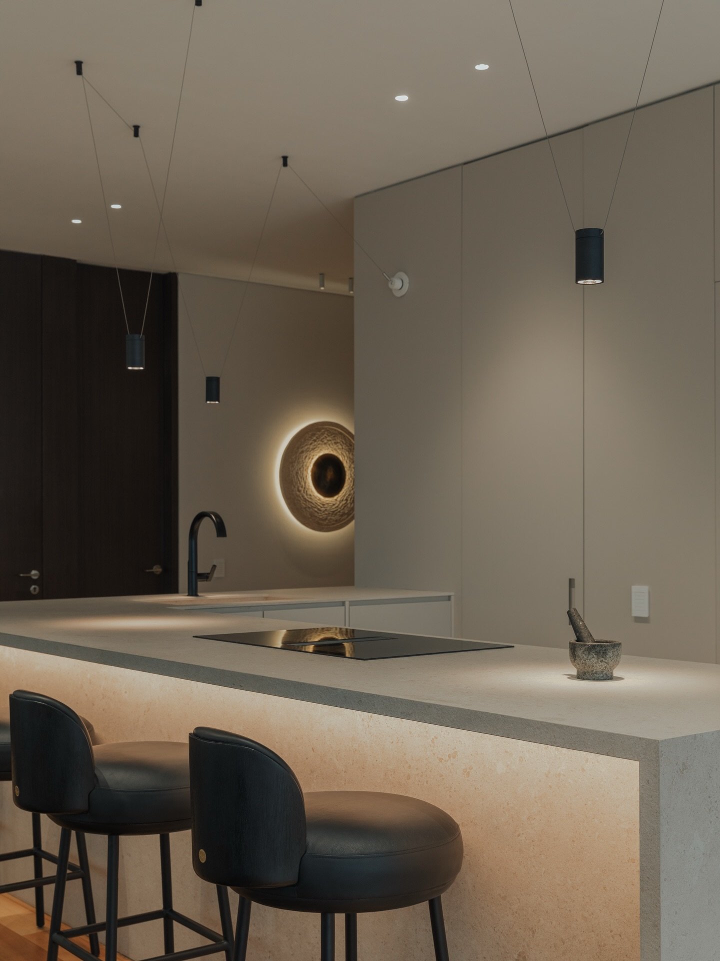 Three small black cylindrical pendants hanging by thin wires over a lit concrete island.