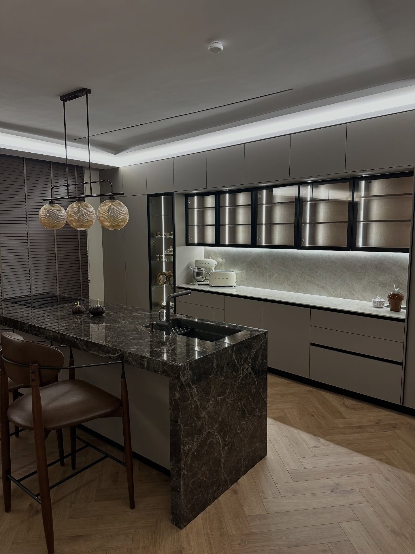 Modern kitchen featuring textured glass pendant lights over a dark marble island and illuminated glass cabinets.