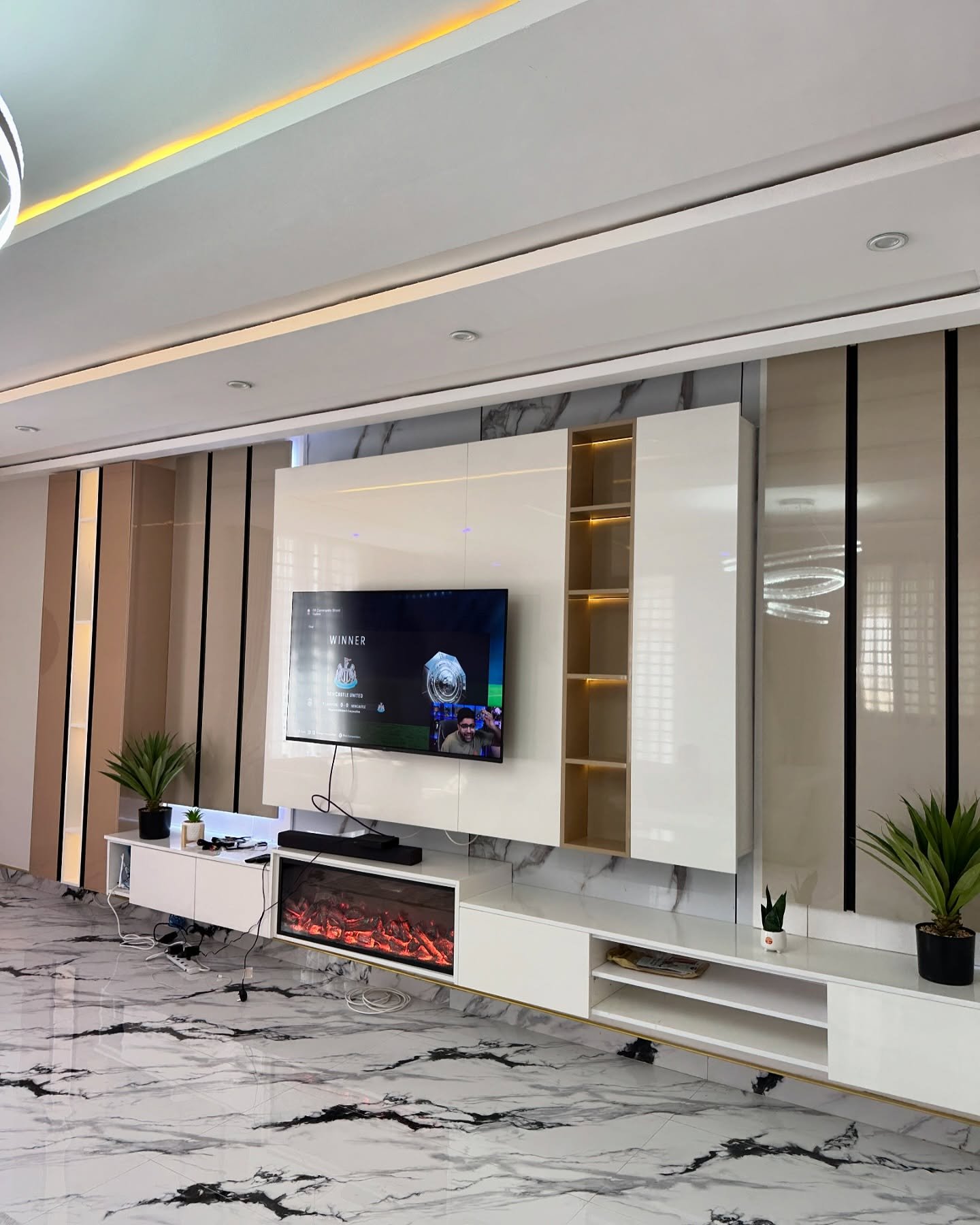High-gloss white TV wall with beige side panels, open shelving, and electric fireplace.