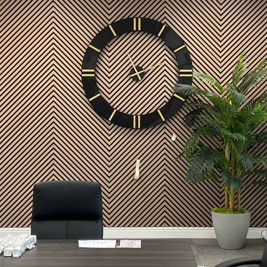 Large black wall clock mounted on a wooden chevron slat accent wall in a home office