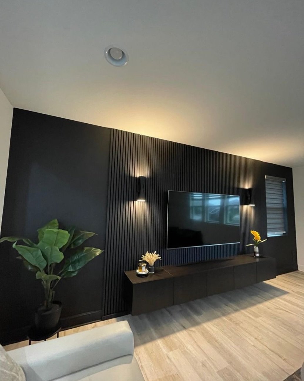 Black accent wall with vertical slats, wall sconces, and floating dark console.