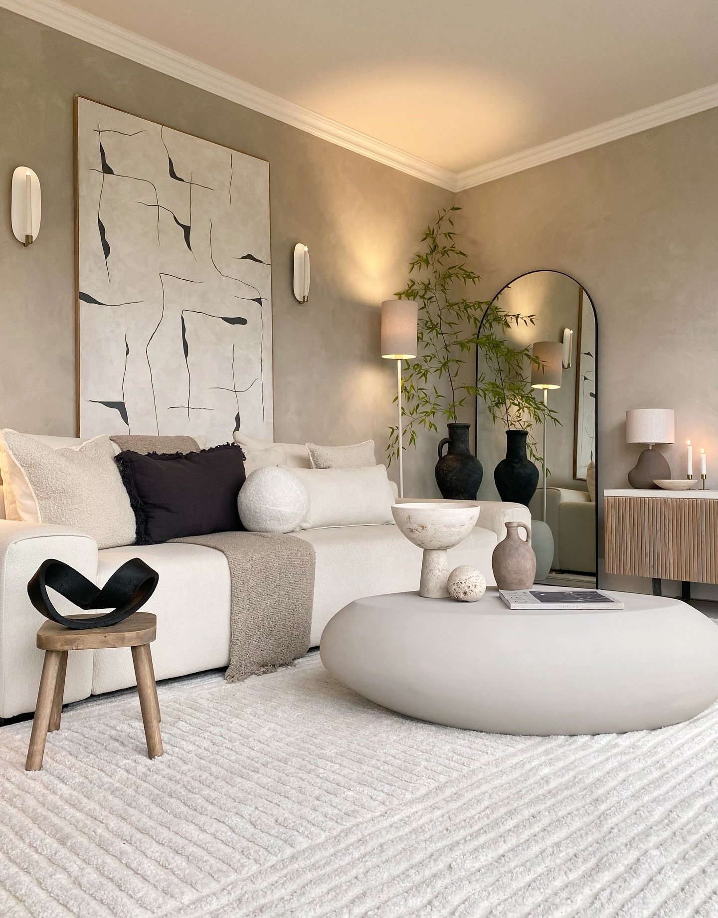 Beige living room featuring limewash textured walls, large black and white abstract art, and an arched mirror.