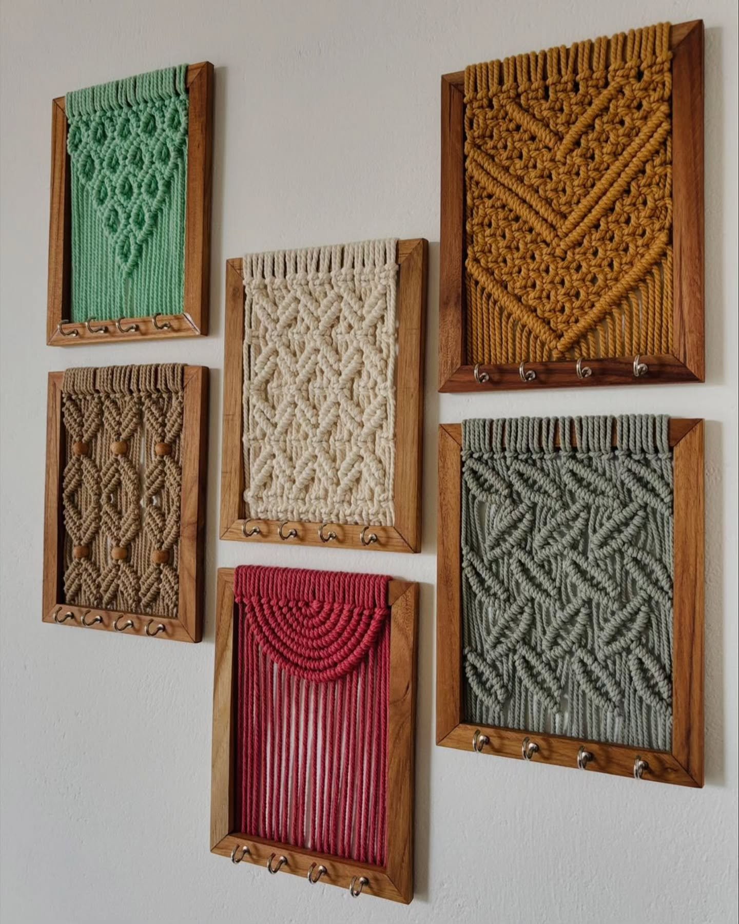 Gallery wall of six colorful framed macrame art pieces with key hooks on a white wall