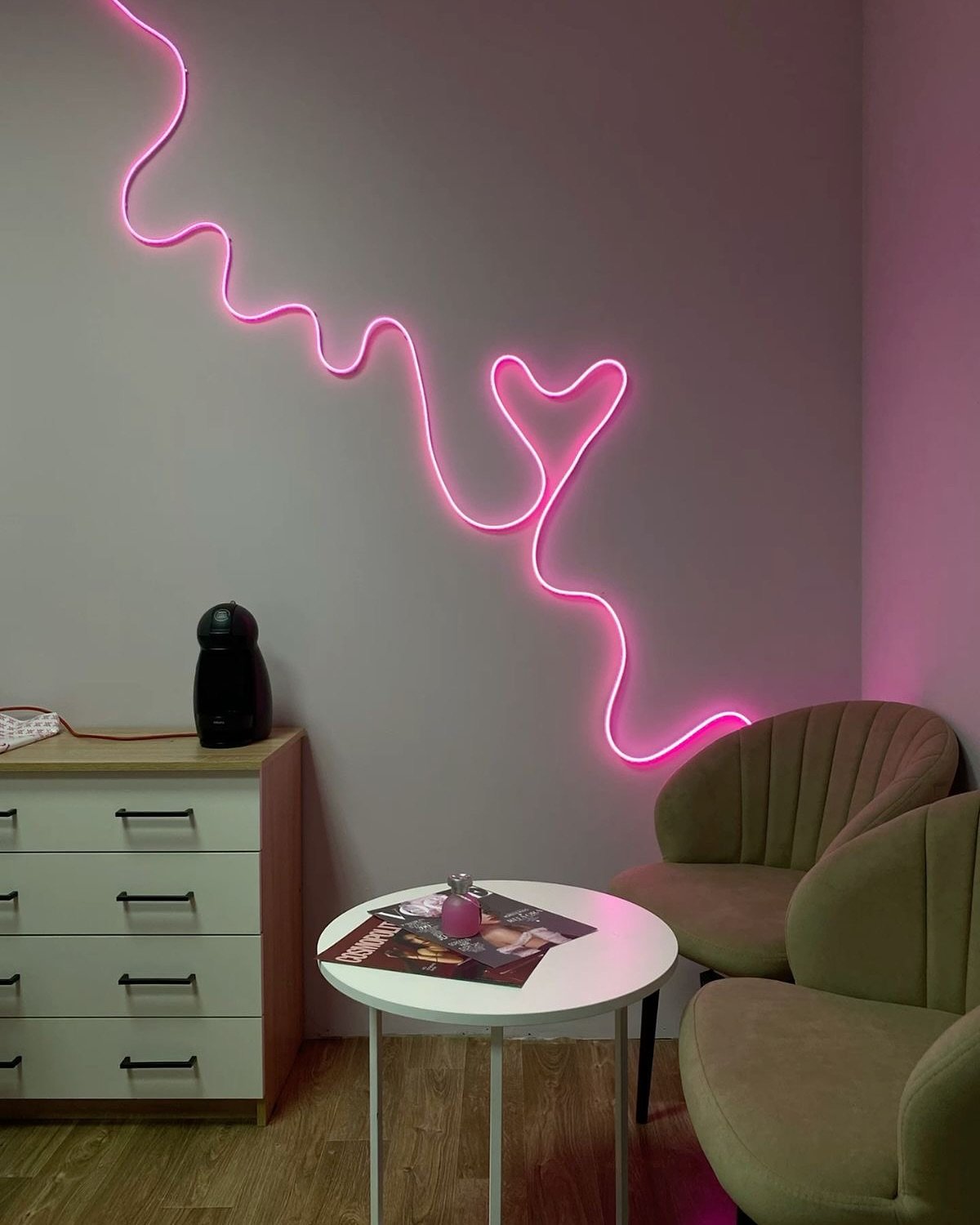 Corner of a room featuring a pink neon LED strip shaped into a wavy line and heart on a plain wall.