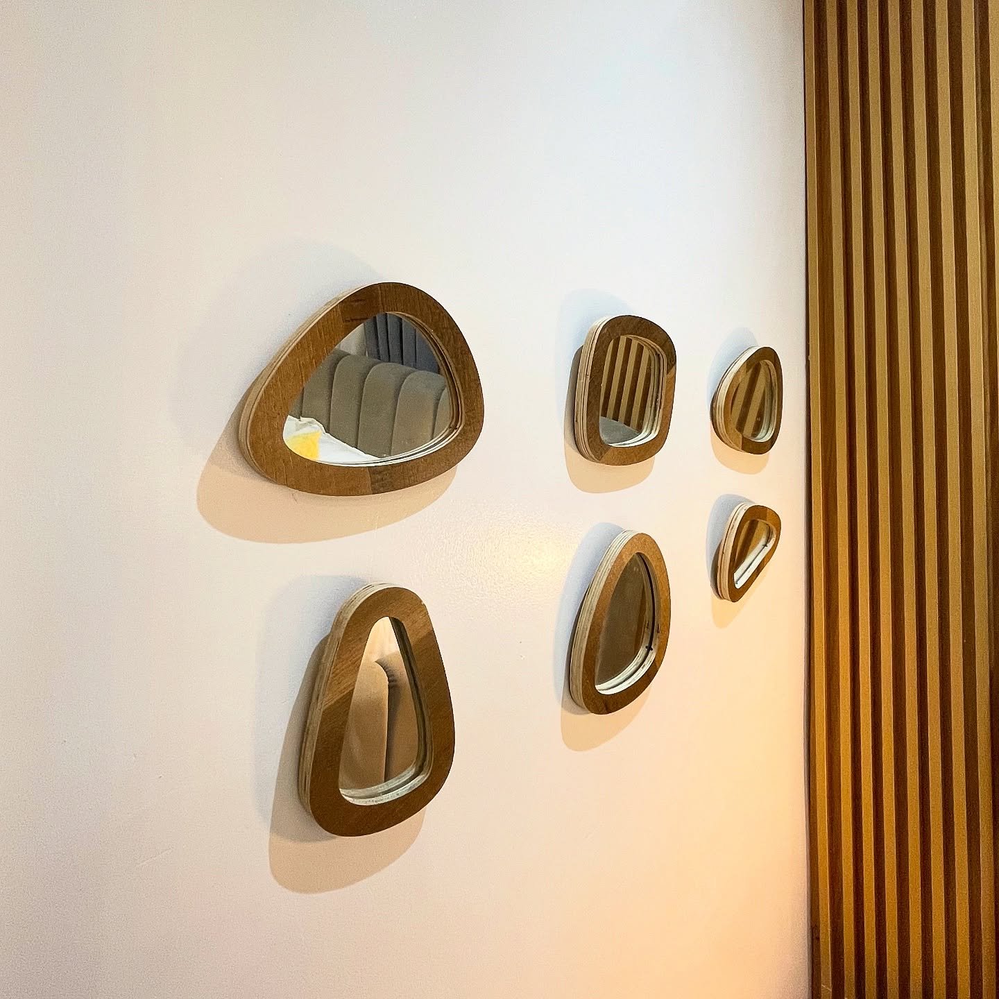 Cluster of small organic wooden framed mirrors arranged on a white wall next to vertical wood slats.