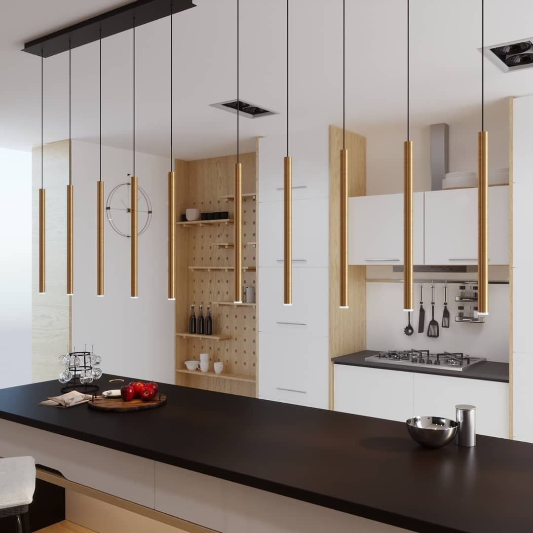 Row of thin gold cylinder lights hanging over a long dark kitchen island.