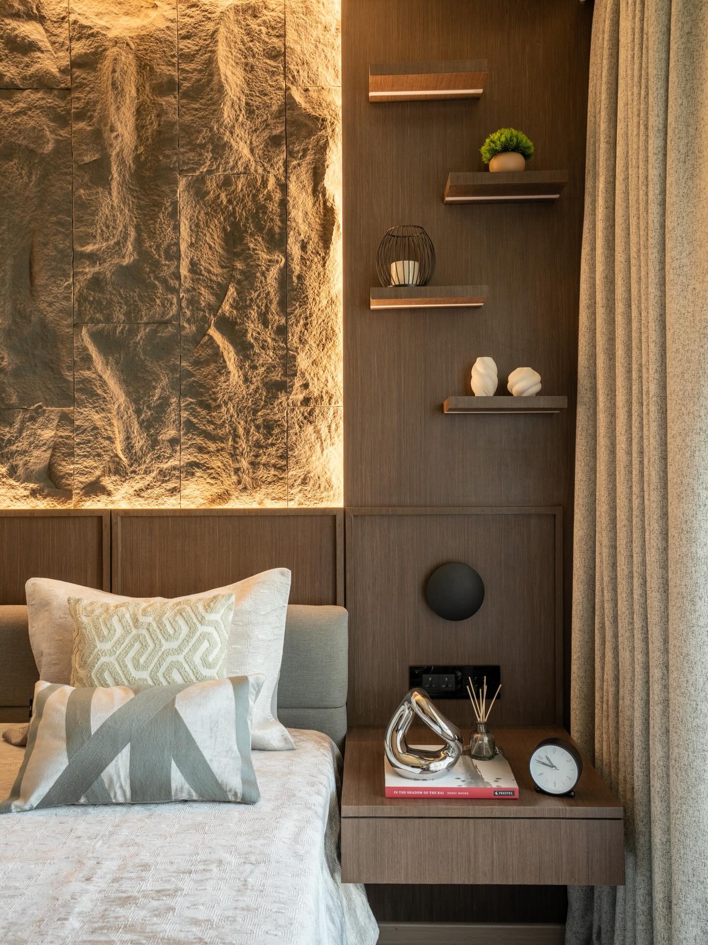 Bedroom featuring a rough stone accent wall illuminated by uplighting next to dark wood paneling with shelves.
