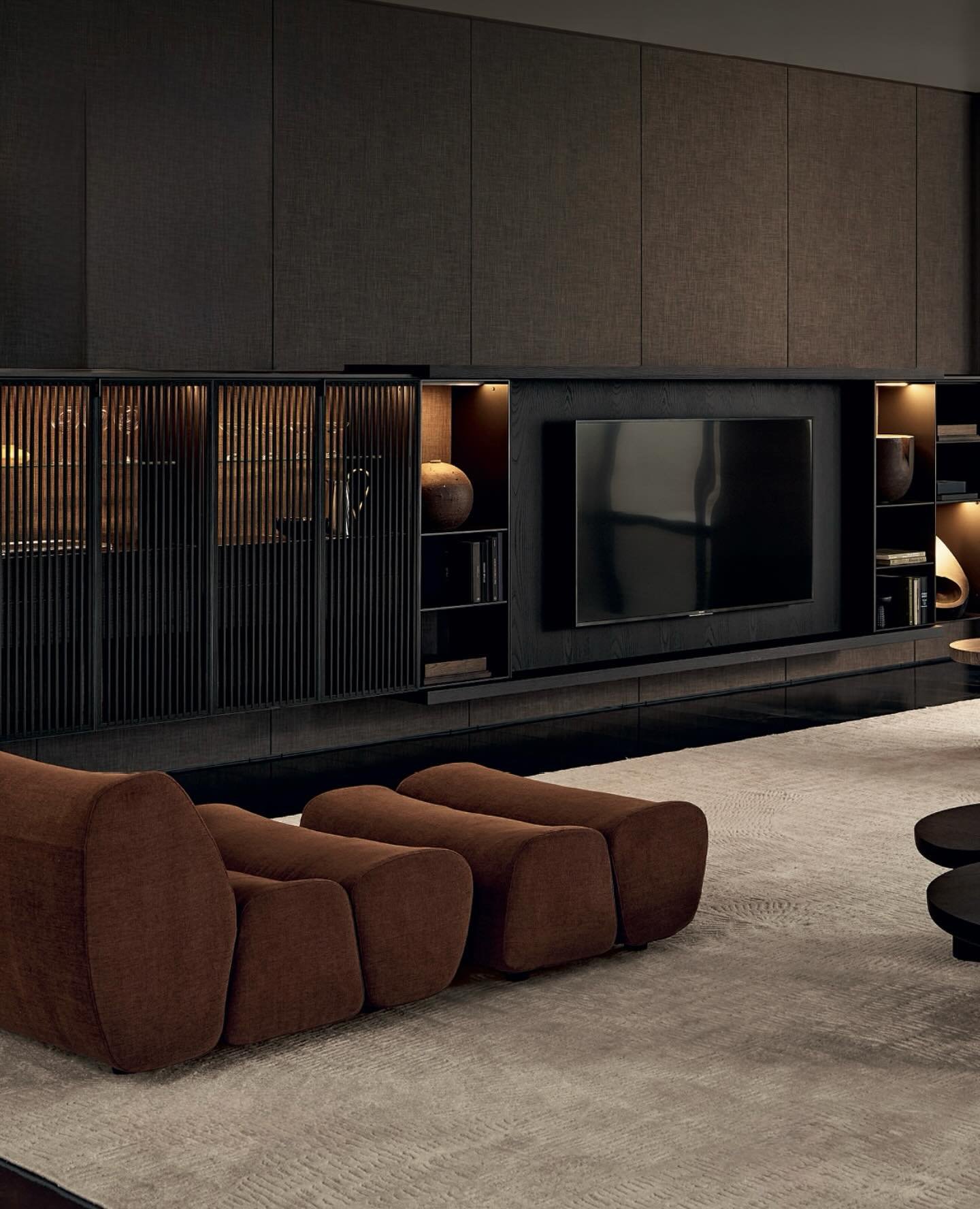 Dark wood TV wall unit with sliding slatted doors, illuminated shelves, and brown velvet seating.