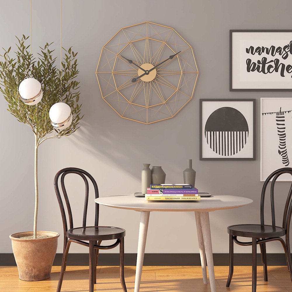 Gold geometric wireframe wall clock mounted on a soft grey wall in a modern dining area
