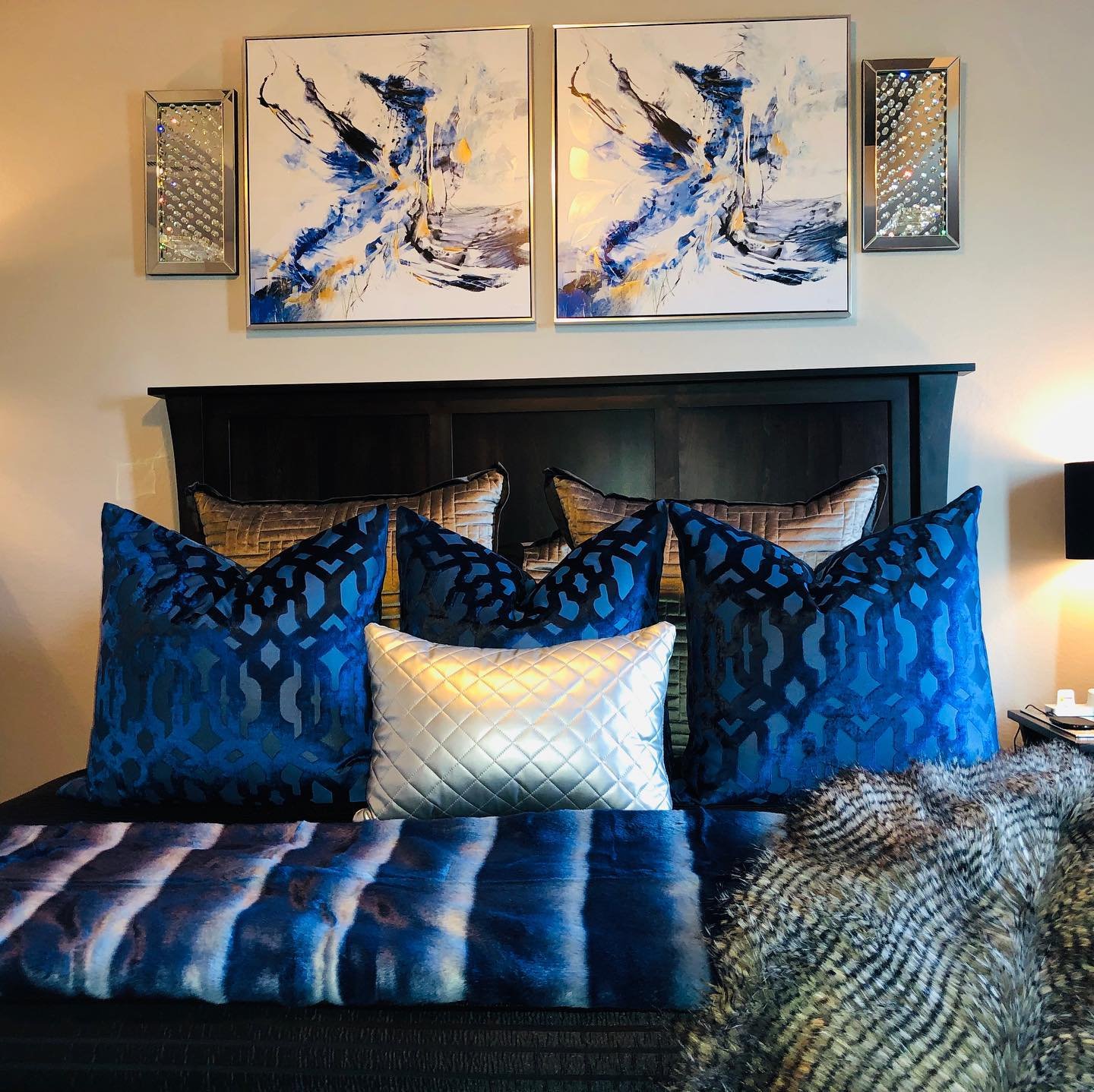 Two blue abstract paintings and mirrored panels above dark wood bed