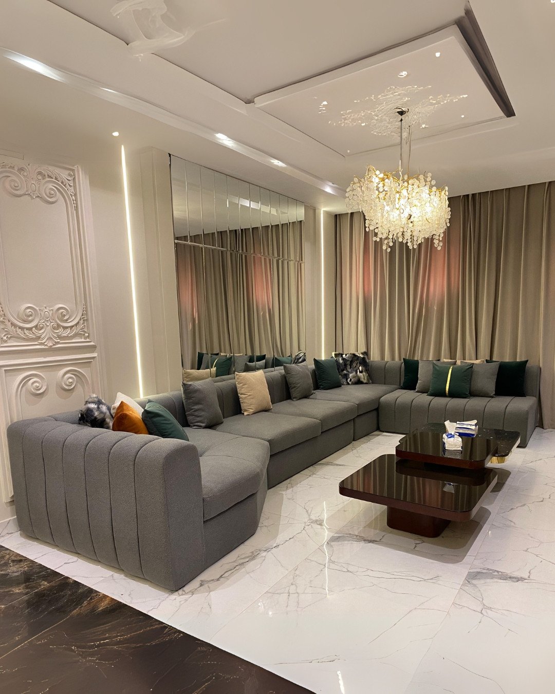 Luxurious living room featuring a gold and crystal branch chandelier hanging from a decorative white ceiling panel.