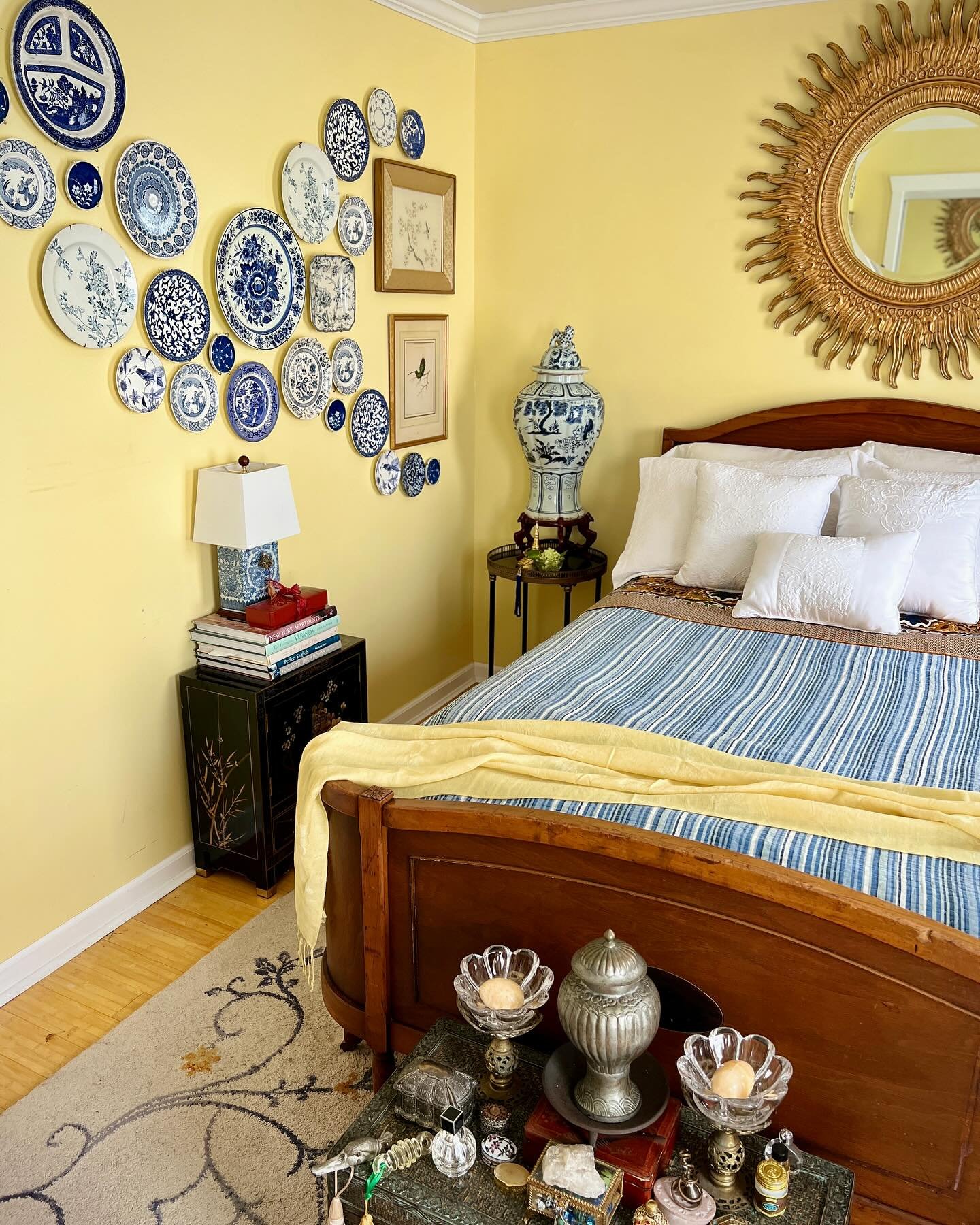 Yellow bedroom wall featuring a cloud-like cluster of blue and white plates next to a wooden bed