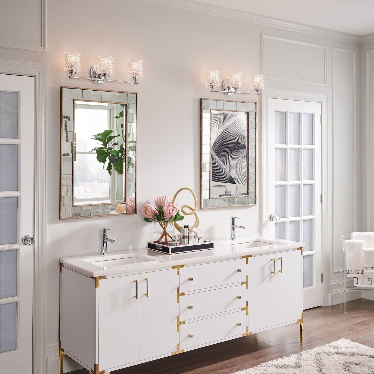 White bathroom accent wall with panel molding, featuring two three-light chrome vanity fixtures above large rectangular mirrors.