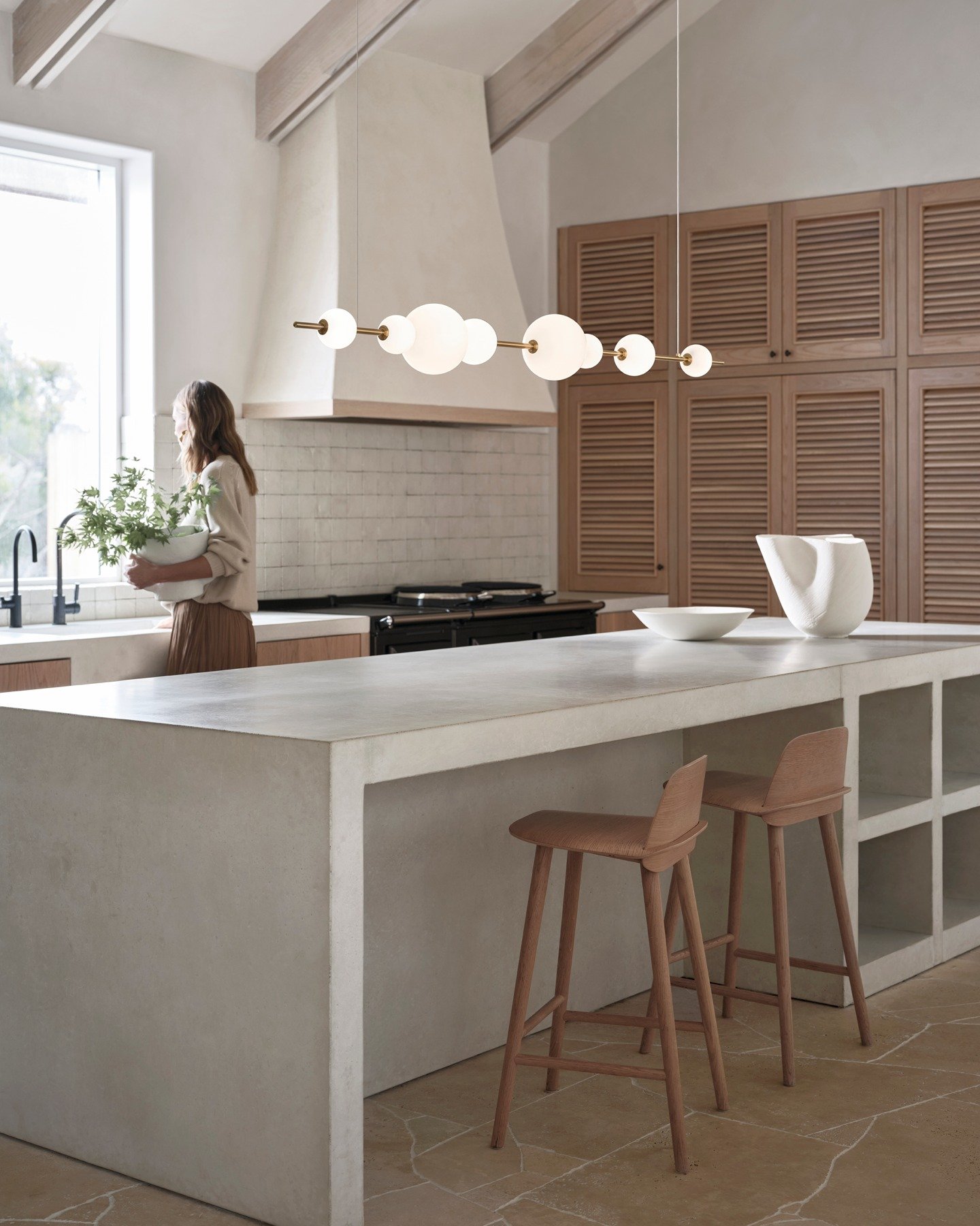 Horizontal brass fixture with white glass orbs hanging over a concrete kitchen island.