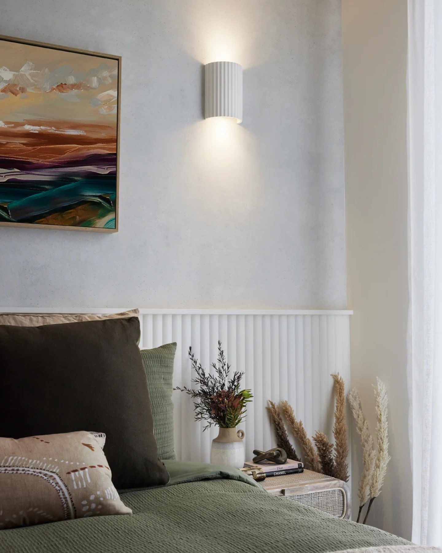Split-texture bedroom accent wall featuring grey plaster and white fluted paneling illuminated by a central white wall sconce.