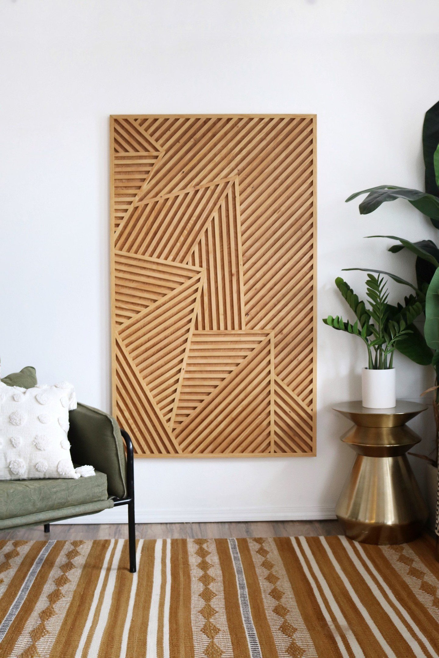 Rectangular wooden wall art with diagonal slat patterns on white wall near green chair