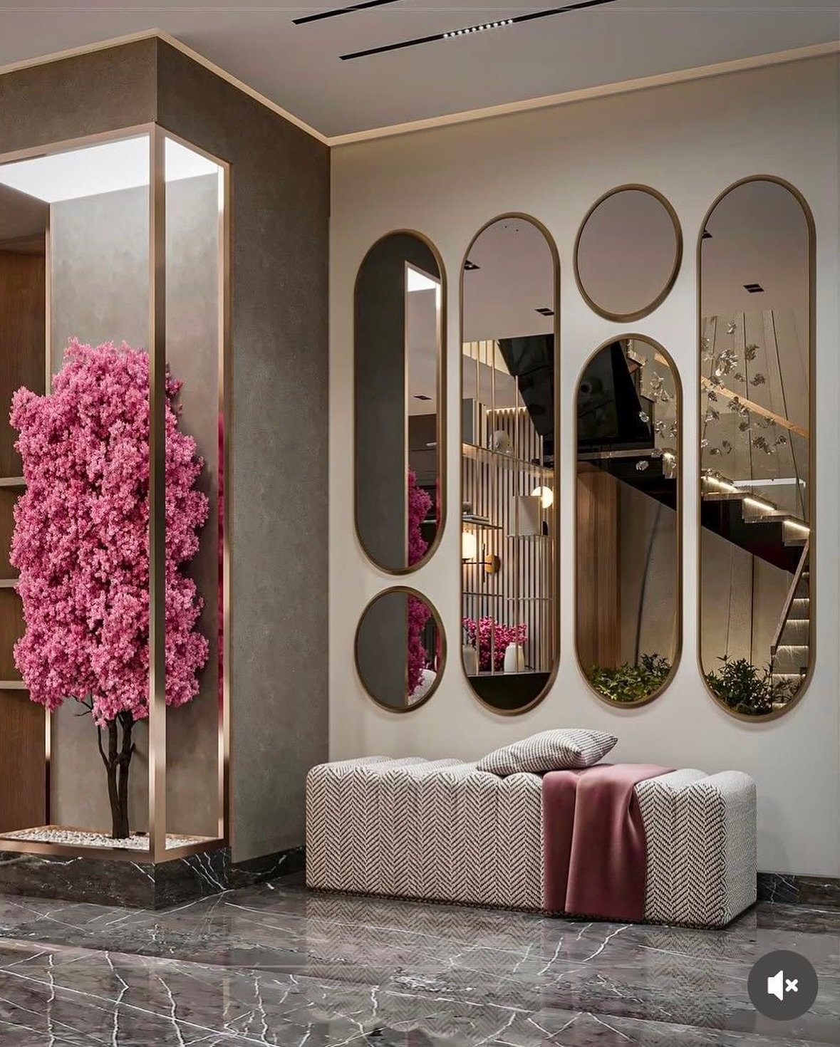 Wall arrangement of tall oval and small round gold mirrors above a patterned bench next to a pink indoor tree.