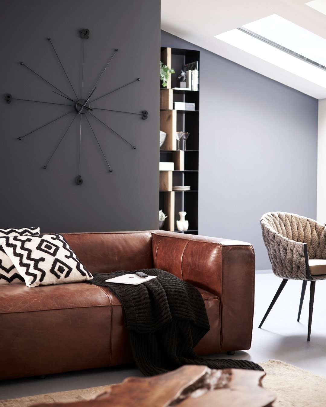 Large black starburst wall clock mounted on a dark charcoal accent wall above a brown leather sofa