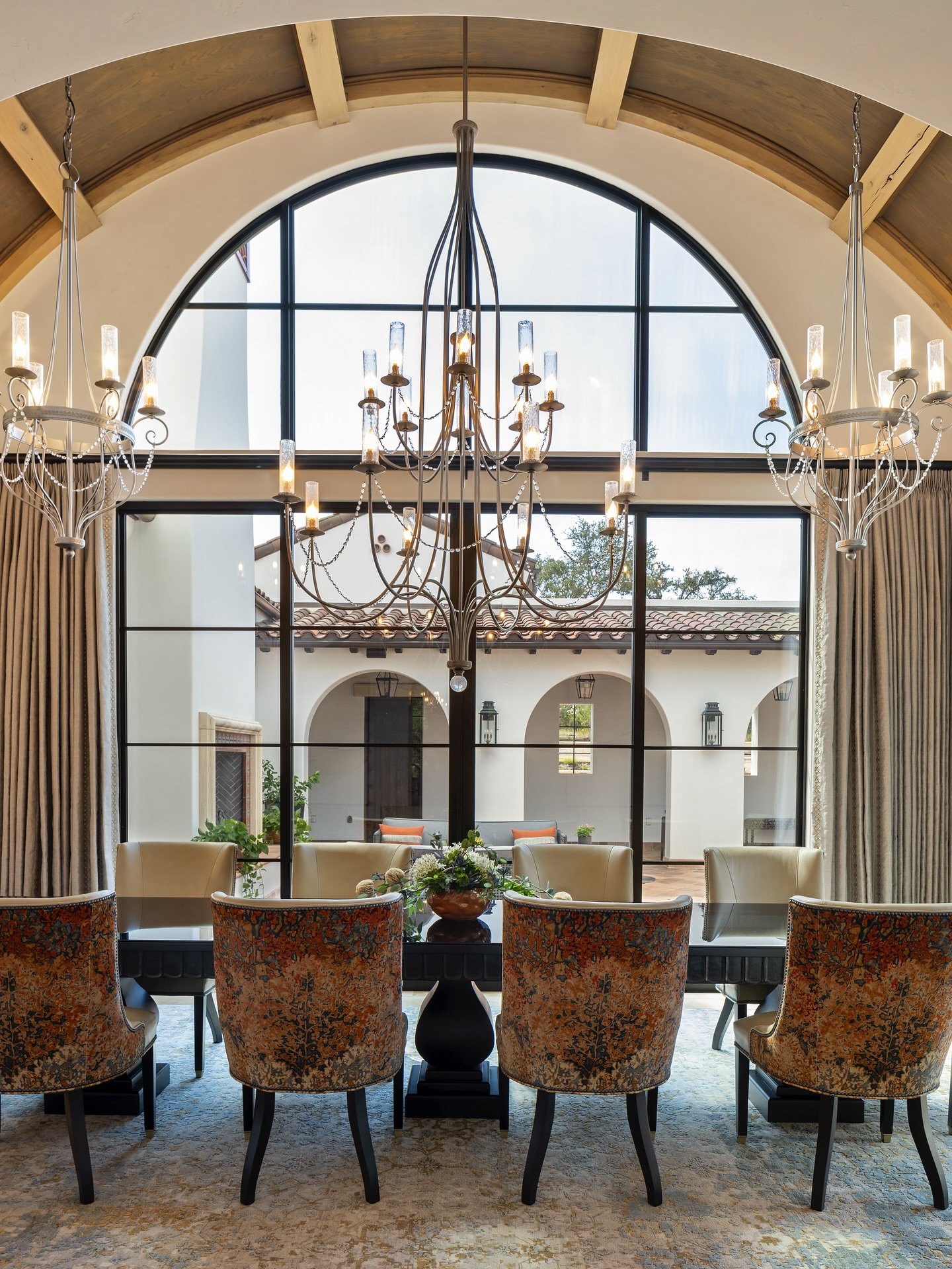 Large iron chandeliers hanging from arched wood beam ceiling in luxury dining room.