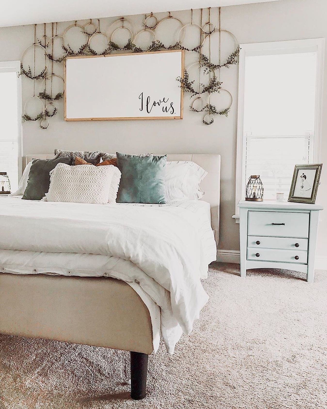 Wooden I love us sign surrounded by embroidery hoops with greenery above bed