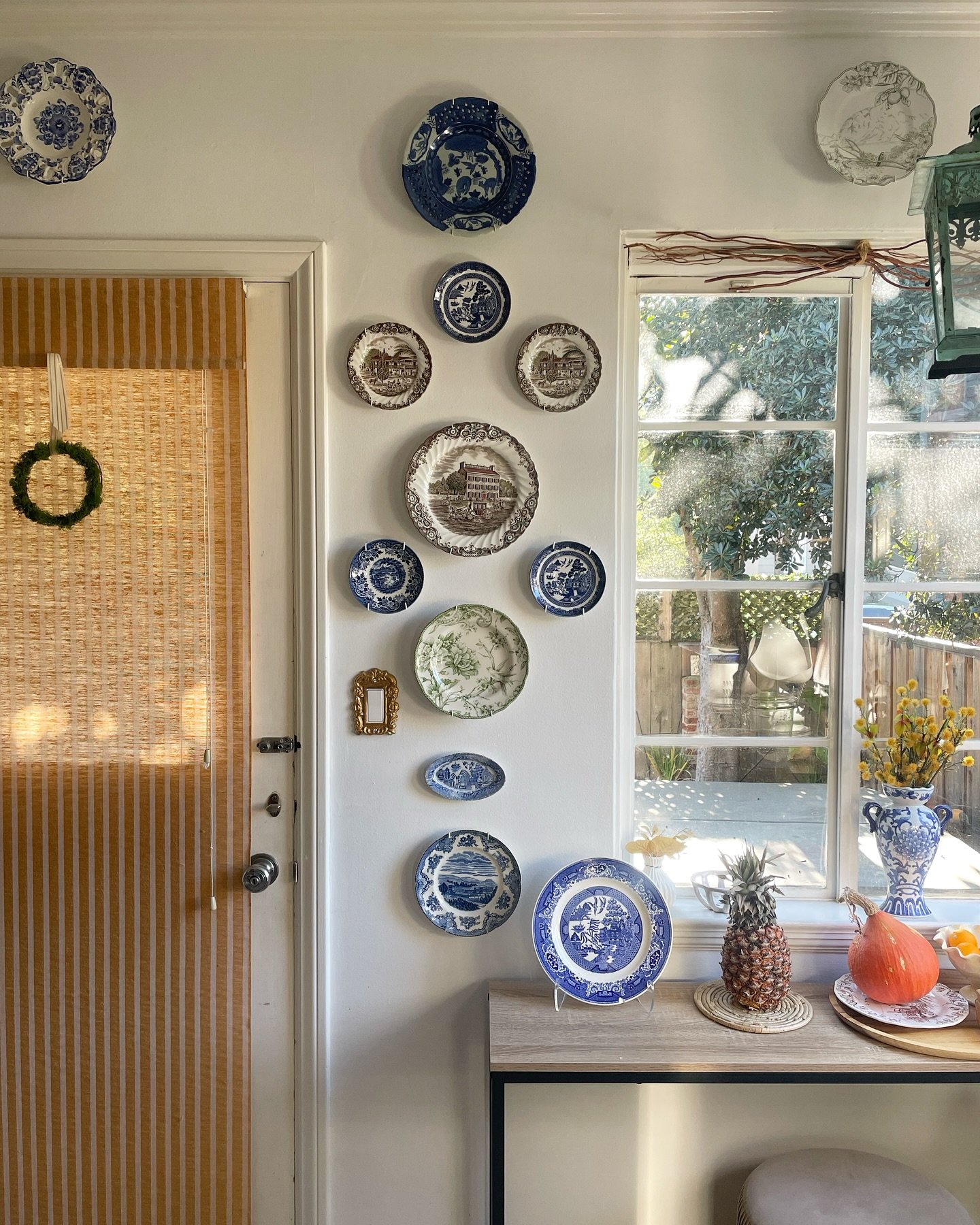 Narrow white wall featuring a vertical stack of blue and brown transferware plates between a door and window