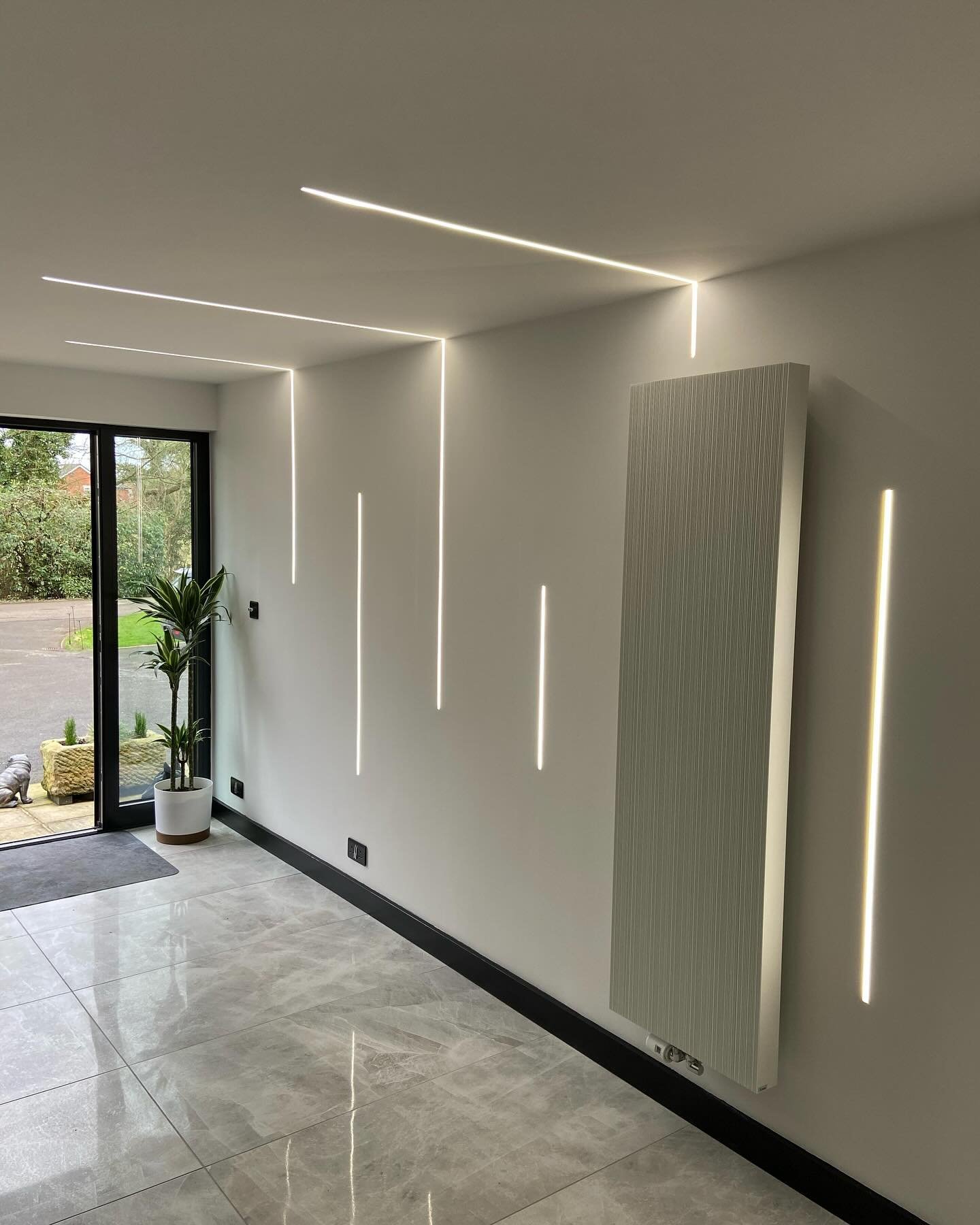 Modern entryway hallway featuring recessed LED strip lights forming vertical lines on white walls that transition seamlessly onto the ceiling.