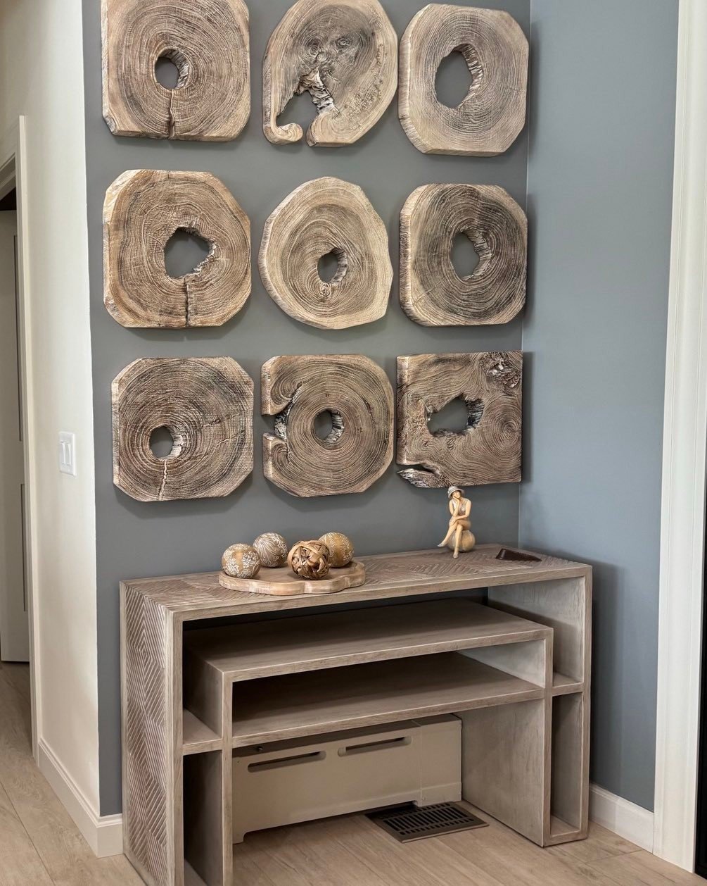 Grid of nine square natural wood slices with hollow centers hanging on a grey wall above a console table