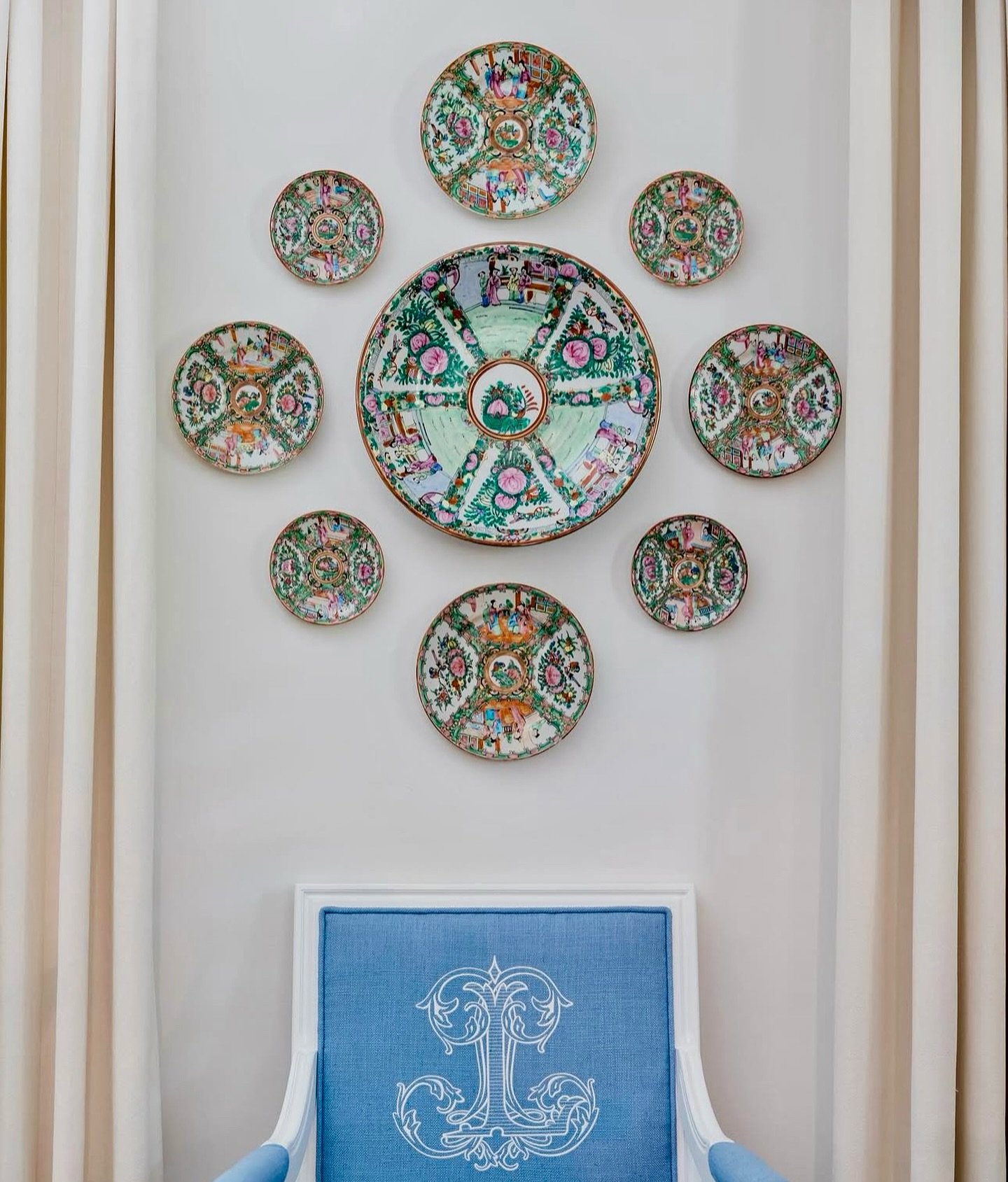 White wall featuring a circular arrangement of pink and green Rose Medallion plates above a blue monogrammed chair