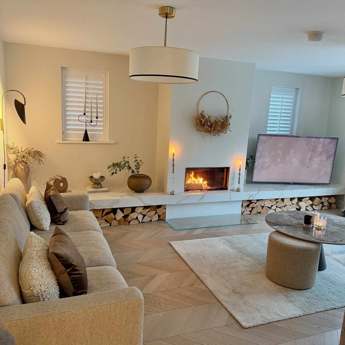 Cozy neutral living room featuring a fabric drum shade pendant light above a herringbone wood floor and fireplace.