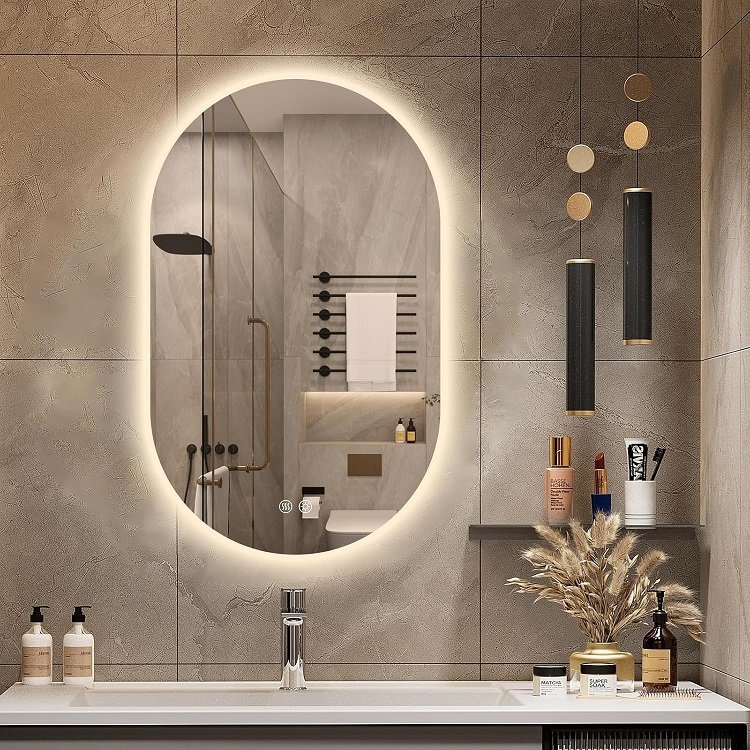 Beige stone tiled bathroom wall featuring large oval backlit mirror and hanging black pendants