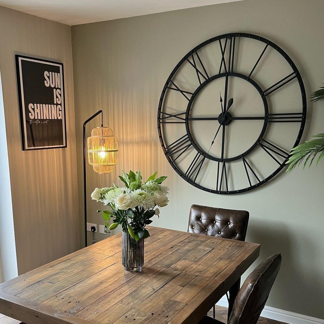 Large black metal skeleton clock with Roman numerals mounted on a sage green dining room wall