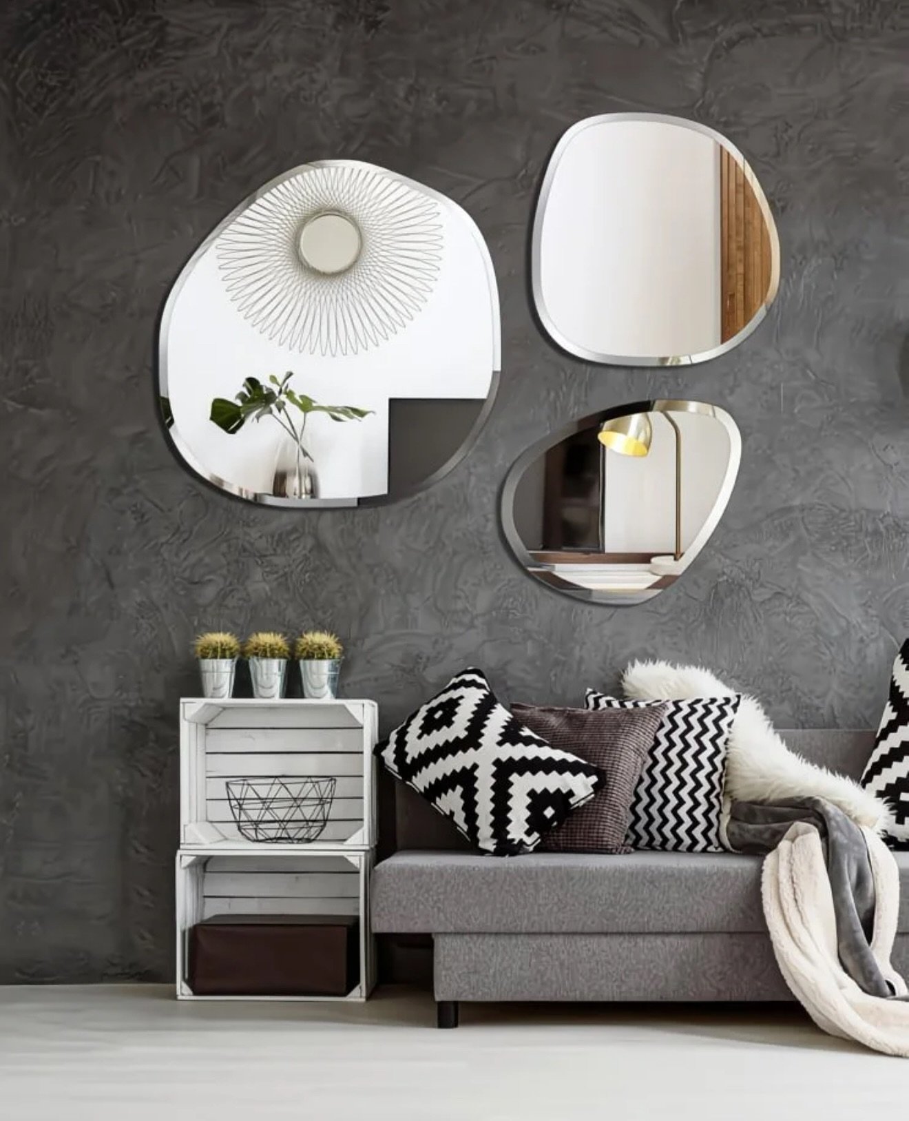 Three organic shaped frameless mirrors arranged on a dark grey textured wall above a modern grey sofa.