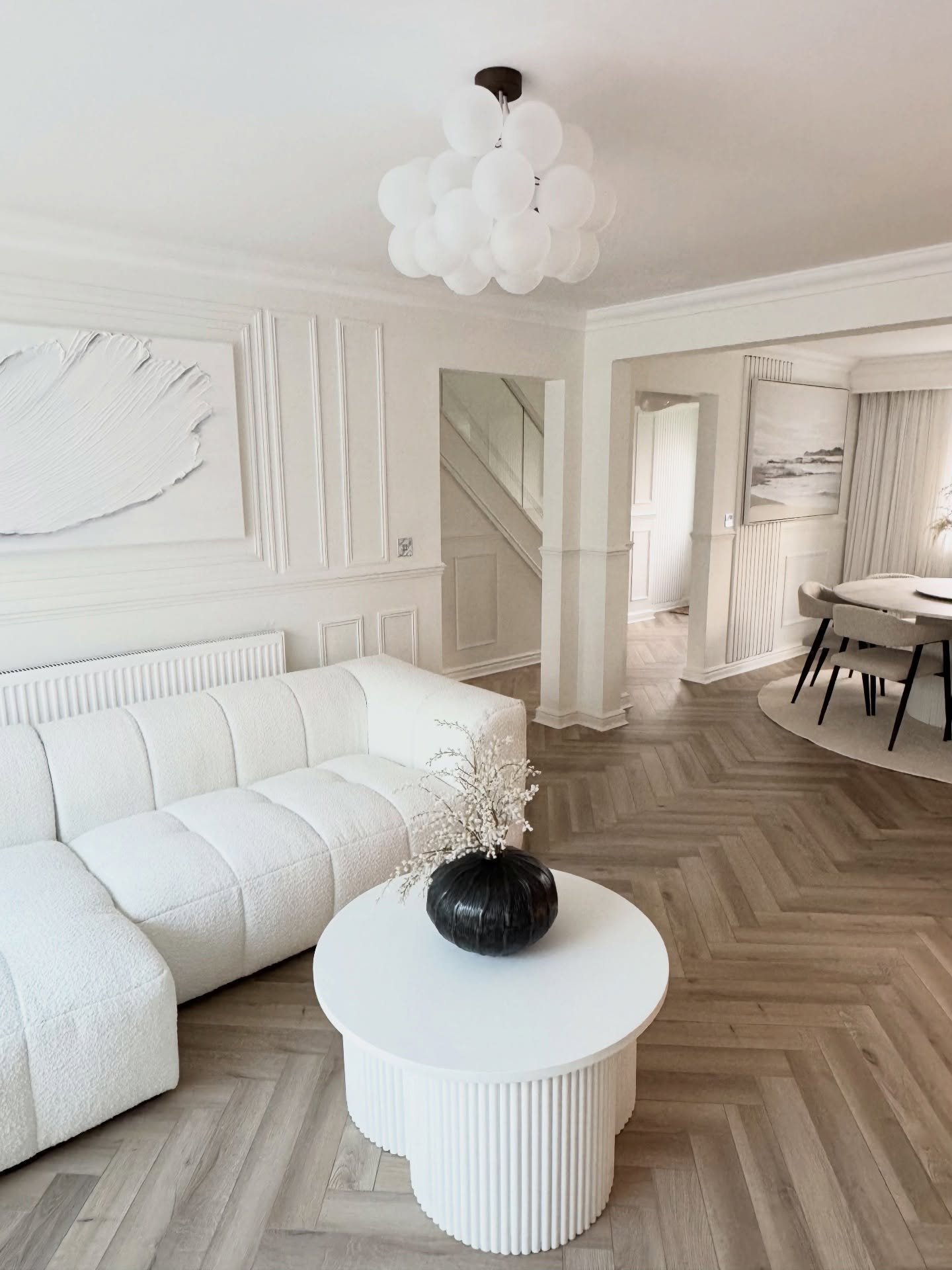 Elegant all-white living room featuring a clustered bubble chandelier above a textured white sofa and herringbone floors.