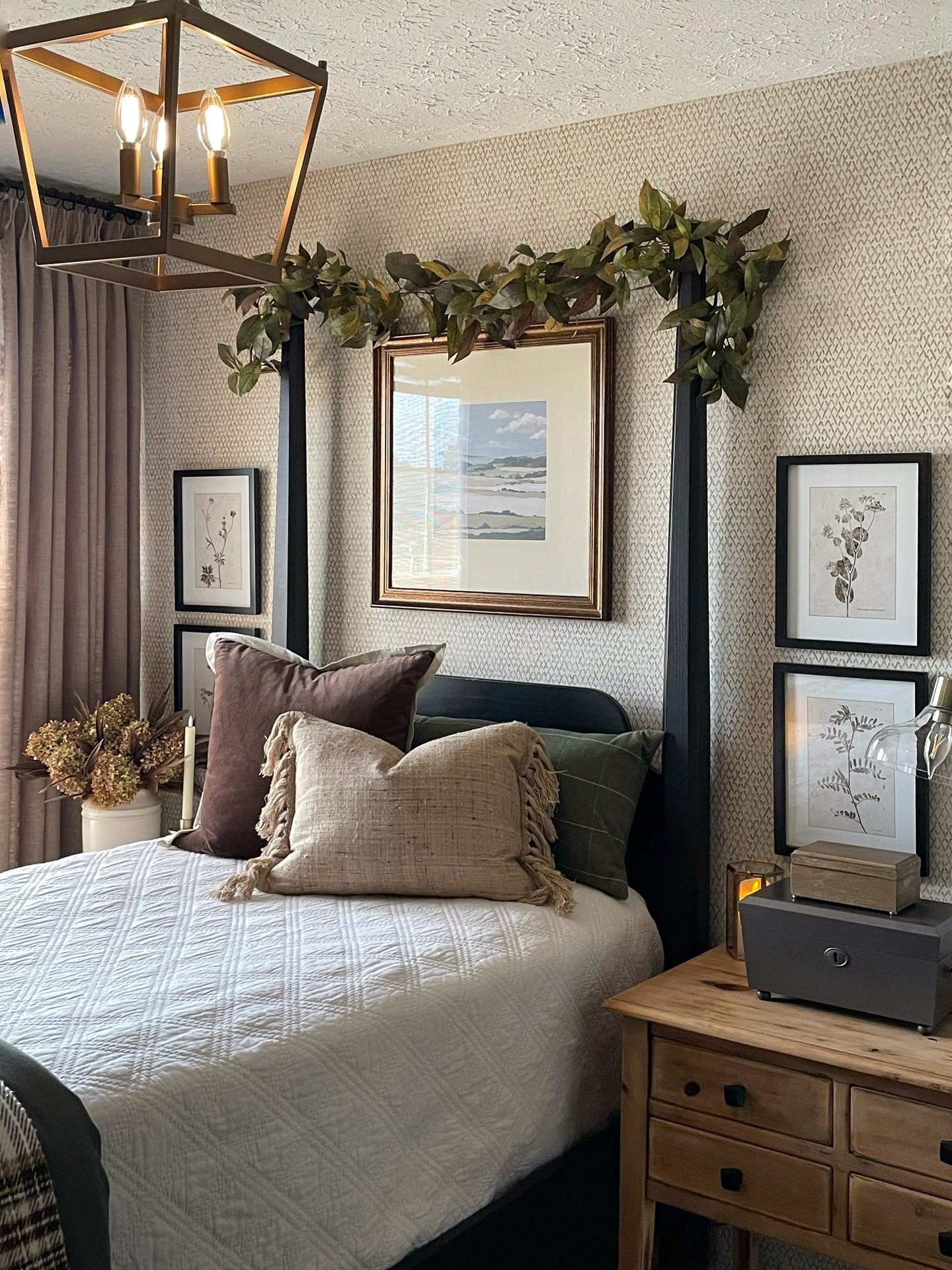 Framed landscape art with garland on patterned wallpaper above four-poster bed