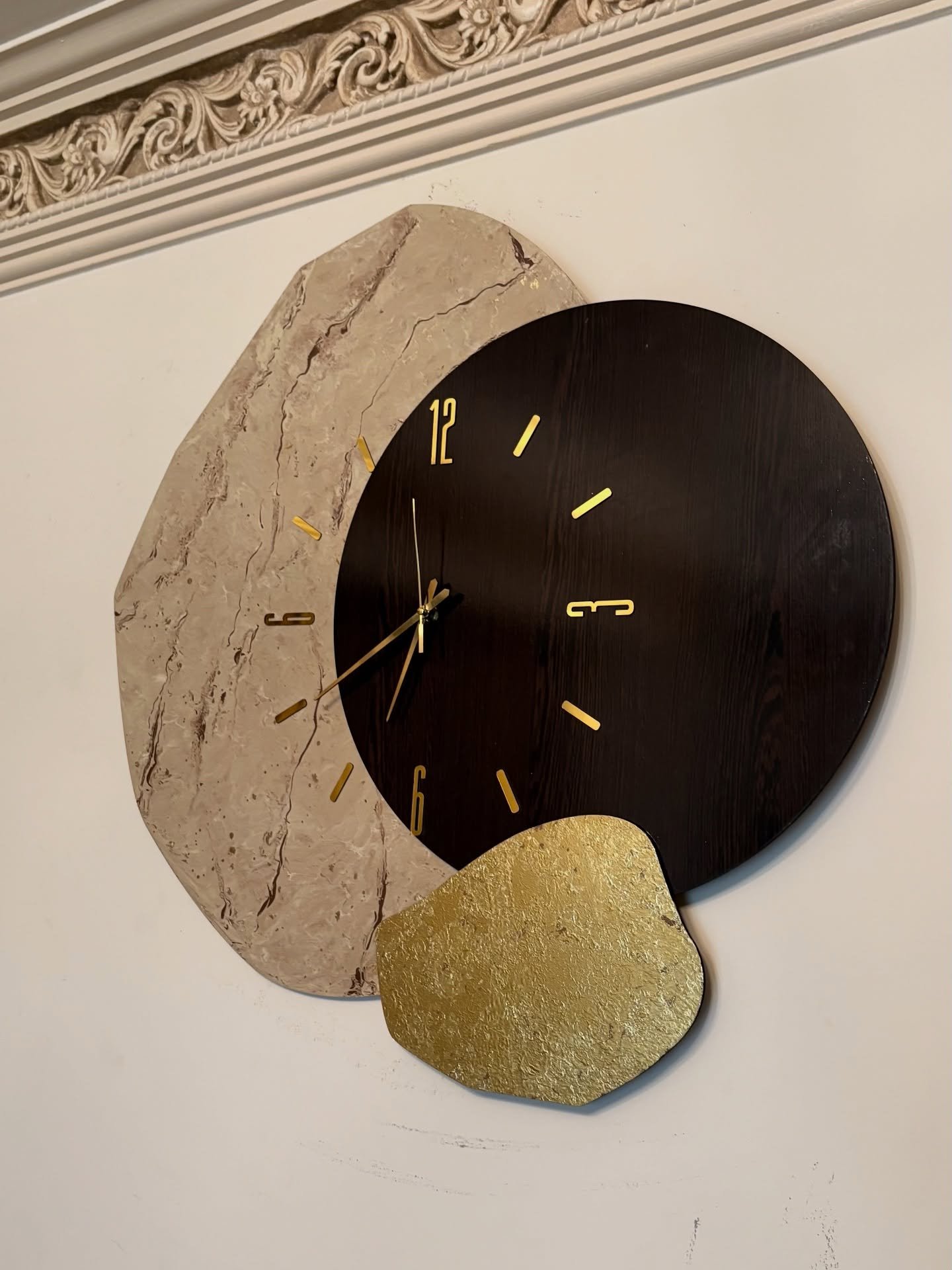 Artistic wall clock with layered marble wood and gold stone shapes on a white wall