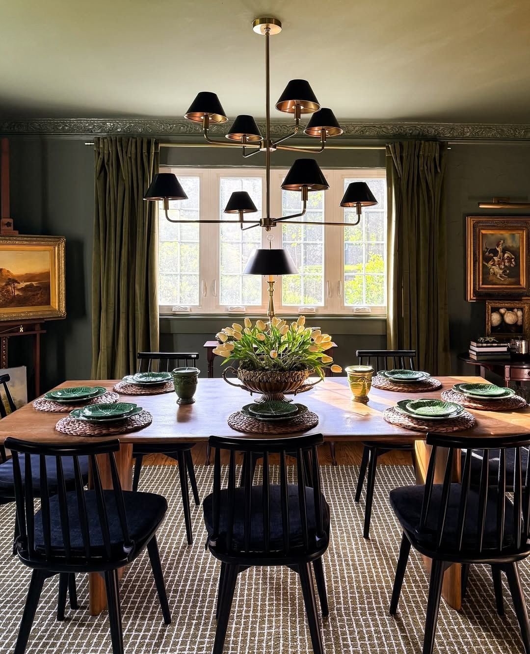 Brass chandelier with black shades in a dark green dining room with spindle chairs.