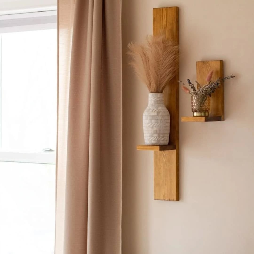 Two vertical wooden wall sconces holding dried flowers and a white vase on a beige wall