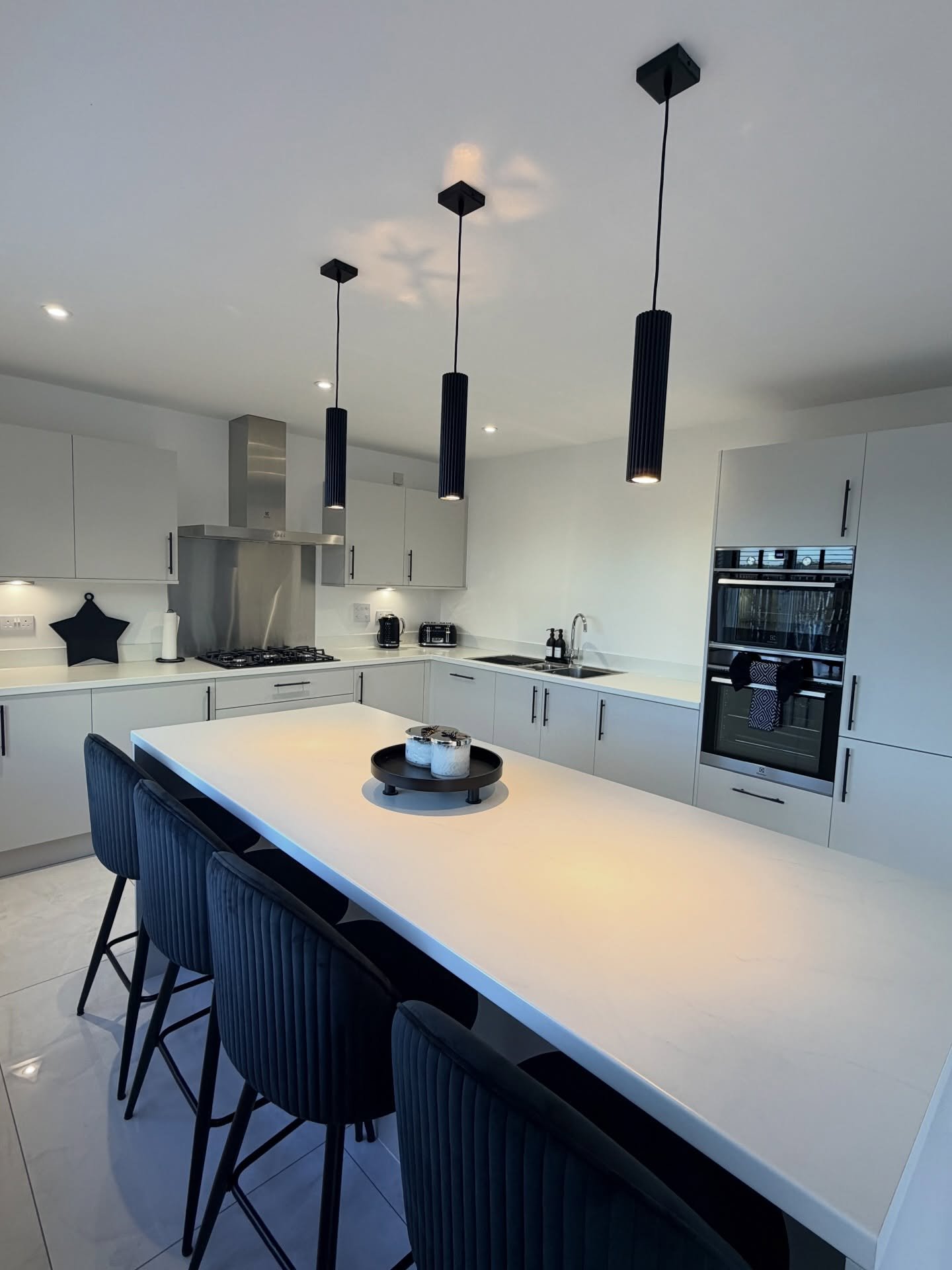 Three ribbed black cylinder lights hanging over a white kitchen island with matching black stools.