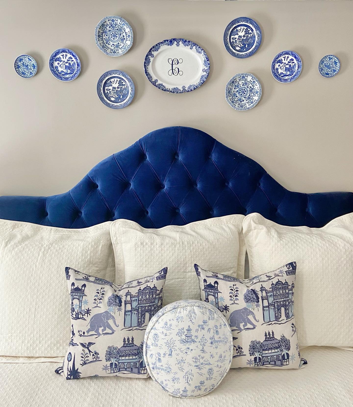 Bedroom wall featuring a curved row of blue and white plates above a navy velvet tufted headboard