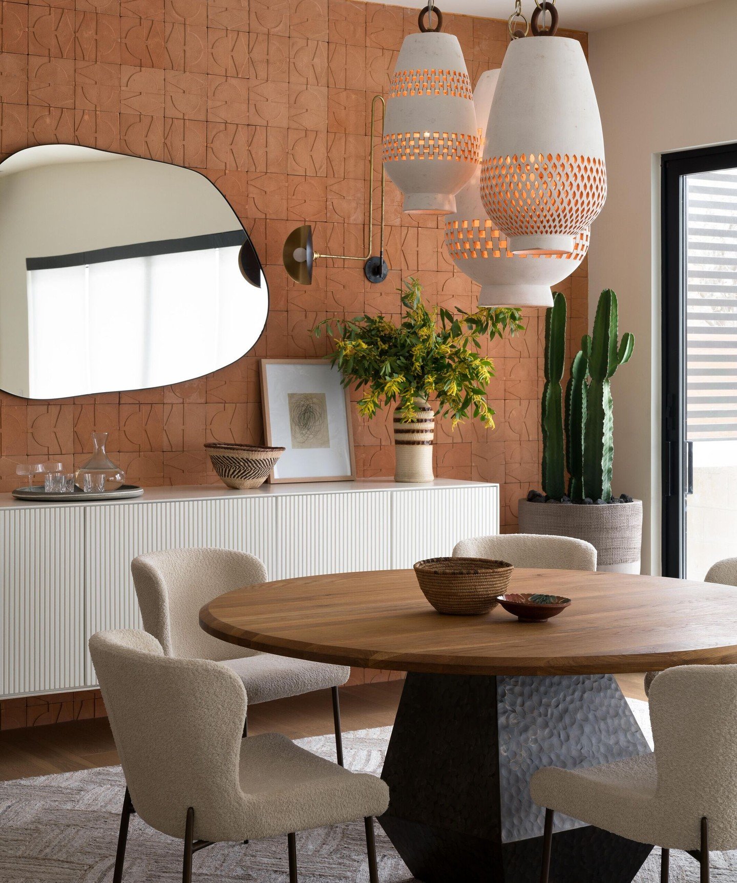 White perforated ceramic pendants over round wood table with terracotta tiled wall.