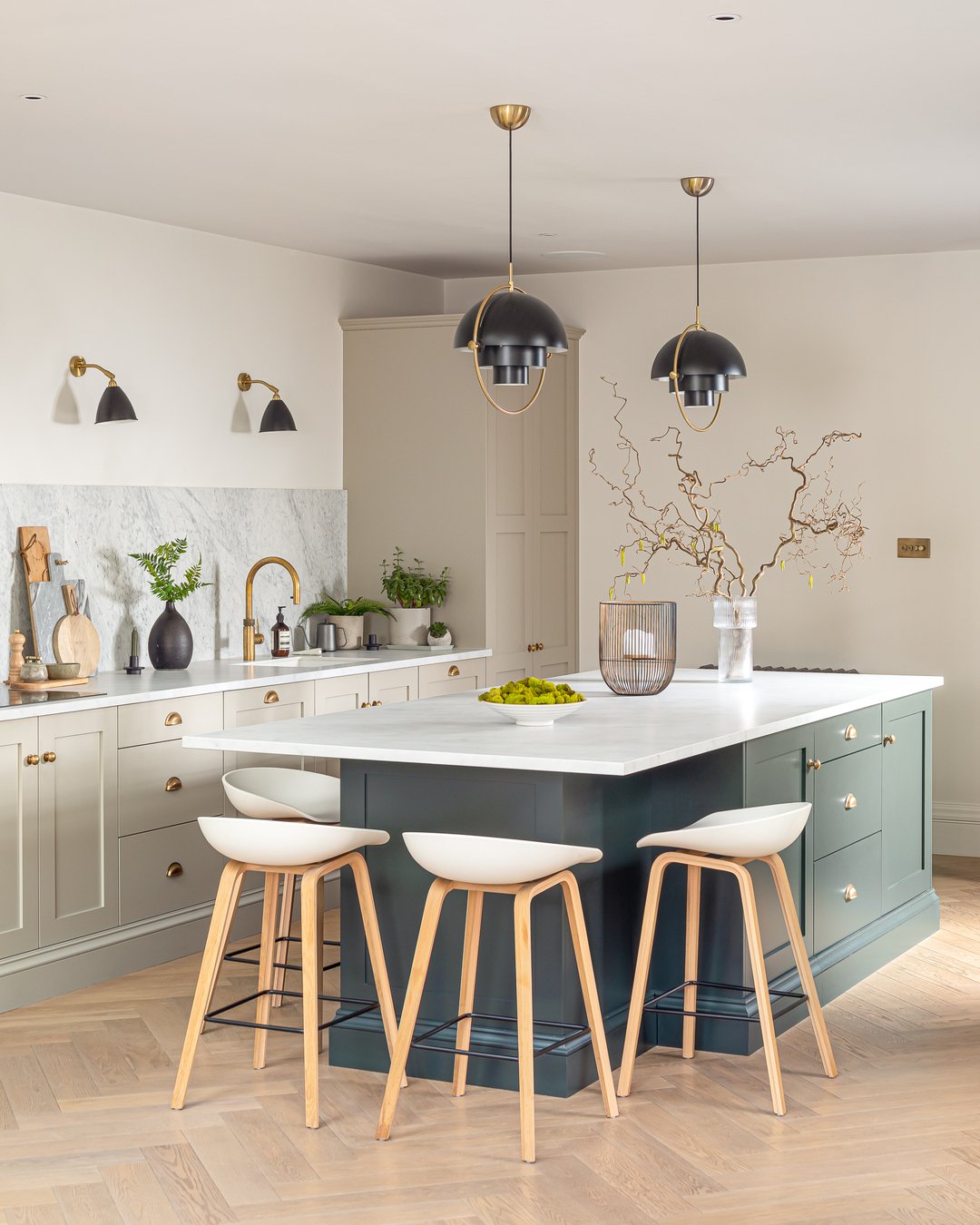 Kitchen island with green cabinetry featuring black pendant lights and brass hardware.
