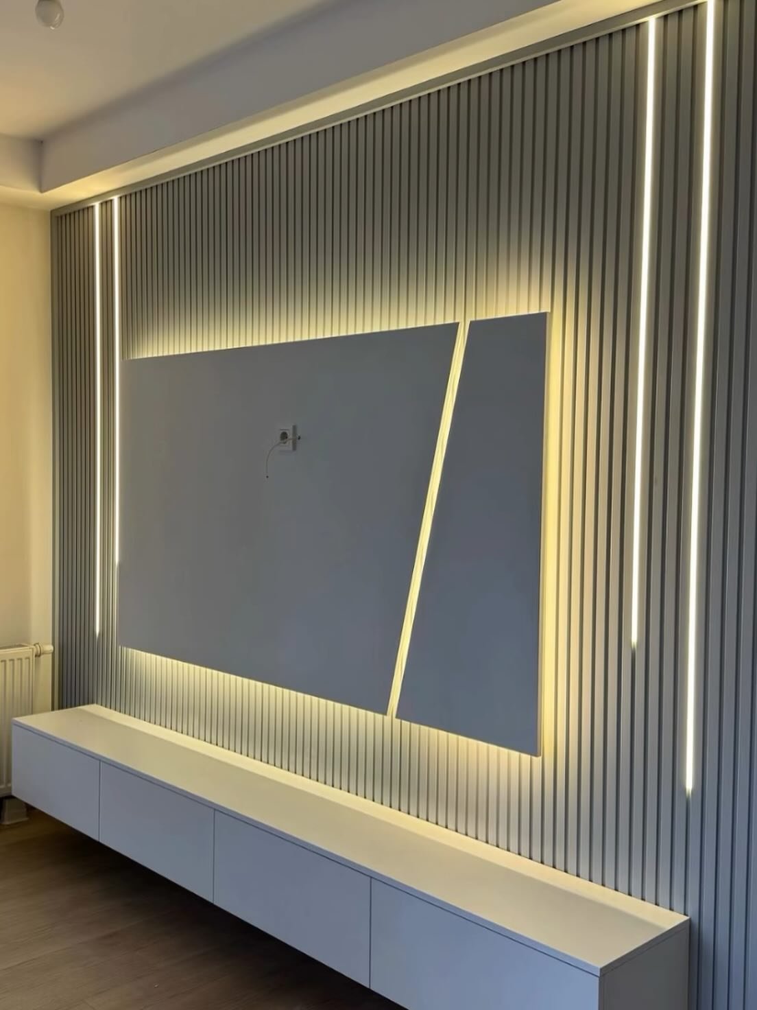 White fluted wall paneling with vertical LED strips and a backlit diagonal split center panel for TV mounting.