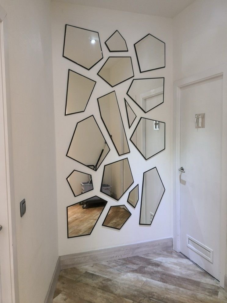 Collage of irregular polygonal mirrors with black frames mounted on a white wall in a hallway next to a white door.