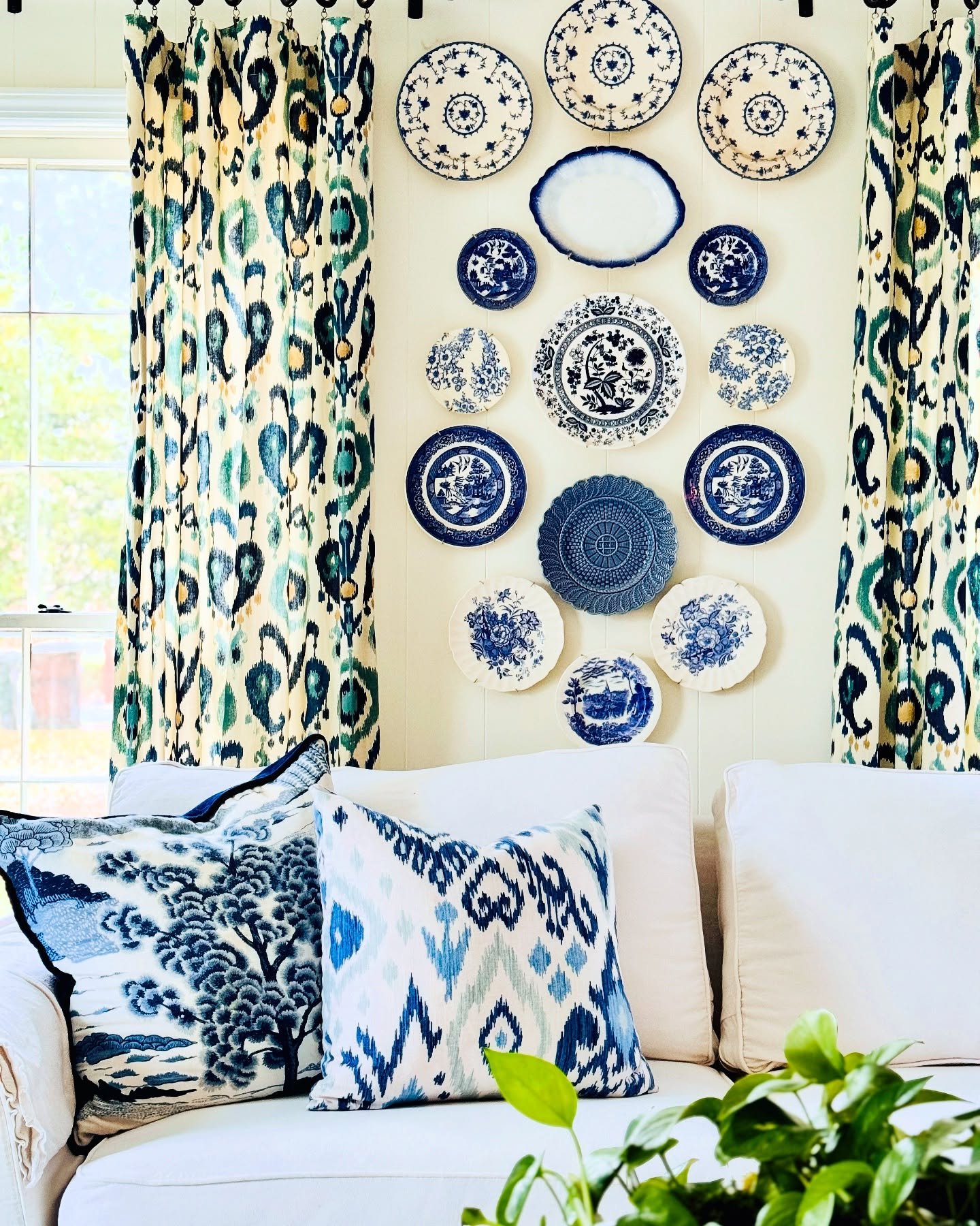 Vertical shiplap wall decorated with a collection of blue and white transferware plates between patterned curtains