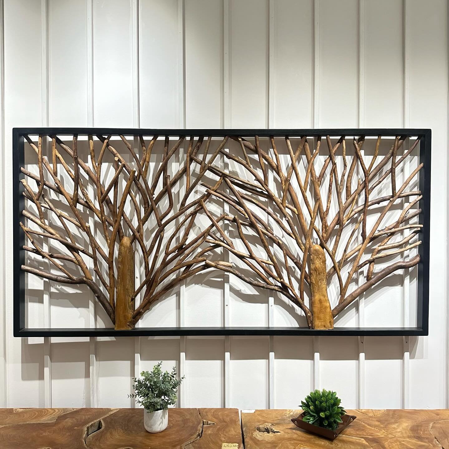 Black framed wall decor featuring natural tree branches mounted on white vertical siding