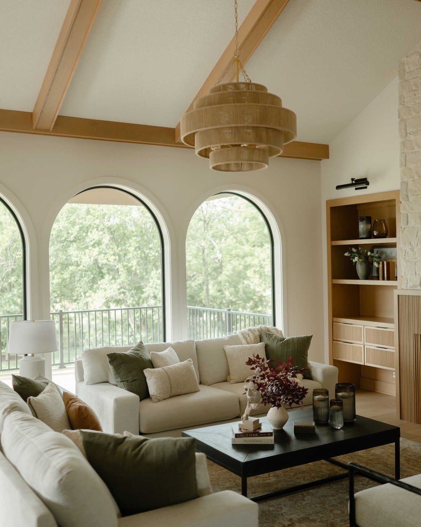 Airy living room featuring a tiered woven rope chandelier hanging from a beamed vaulted ceiling near arched windows.
