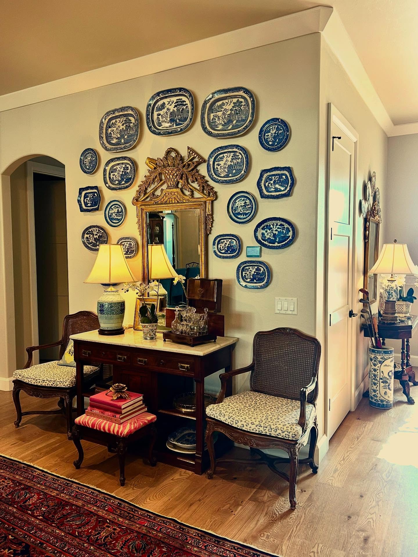 Beige wall featuring a collection of blue and white oval platters surrounding an ornate gold mirror